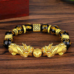 Double Pixiu Obsidian Bracelet – laid on warm wood surface with obsidian mantra beads, Pixiu wealth charm