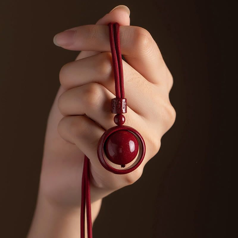 Cinnabar PiXiu Necklace – Hand holding red cord pendant on dark brown background, cinnabar necklace