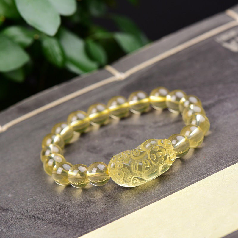 Citrine PiXiu Wealth Bracelet – yellow citrine beads with carved PiXiu on dark book, green leaves, feng shui prosperity
