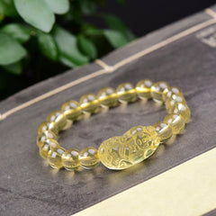 Citrine PiXiu Wealth Bracelet – yellow citrine beads with carved PiXiu on dark book, green leaves, feng shui prosperity