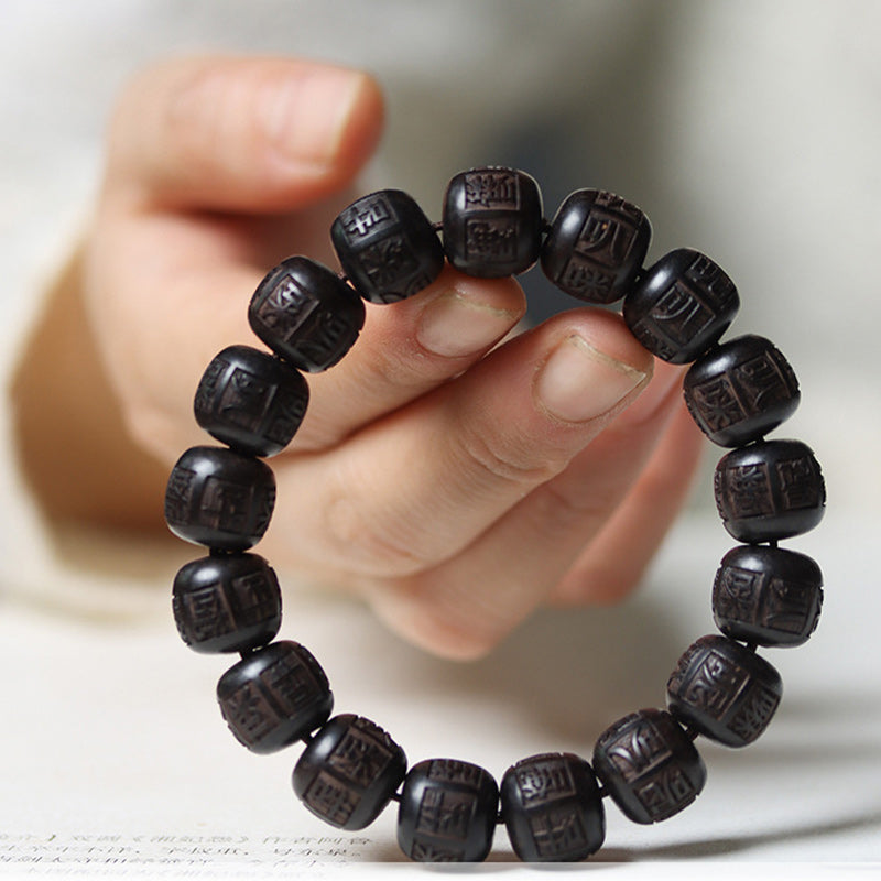 Ebony Wood Mantra Bracelet – Close-up held between fingers revealing engraving detail, Zen jewelry