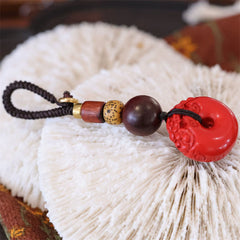 Cinnabar Peace Buckle Keychain – Red pendant with wood and brass beads on white coral texture