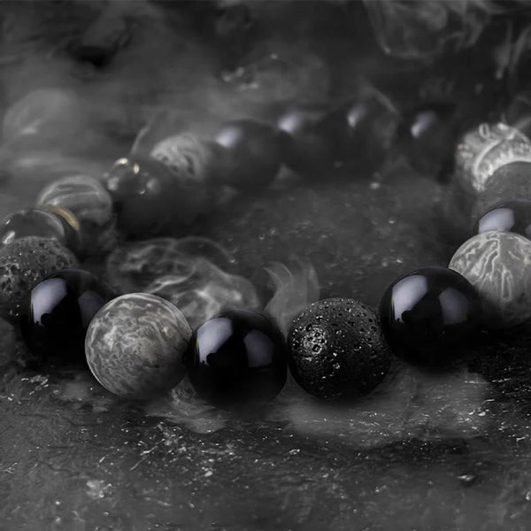 Black Obsidian Lava Rock Yin Yang Bracelet - close-up with atmospheric smoke on dark stone, moody lighting, men jewelry