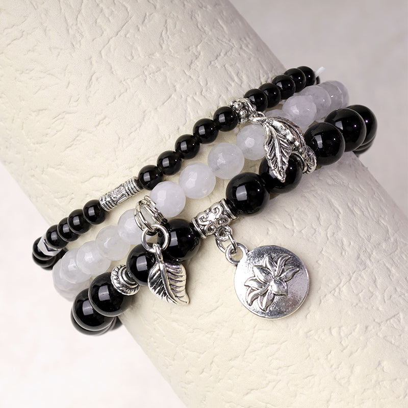 Crystal Lotus Bracelet – glossy black onyx and frosted white quartz on display stand with silver charms, stacking jewelry