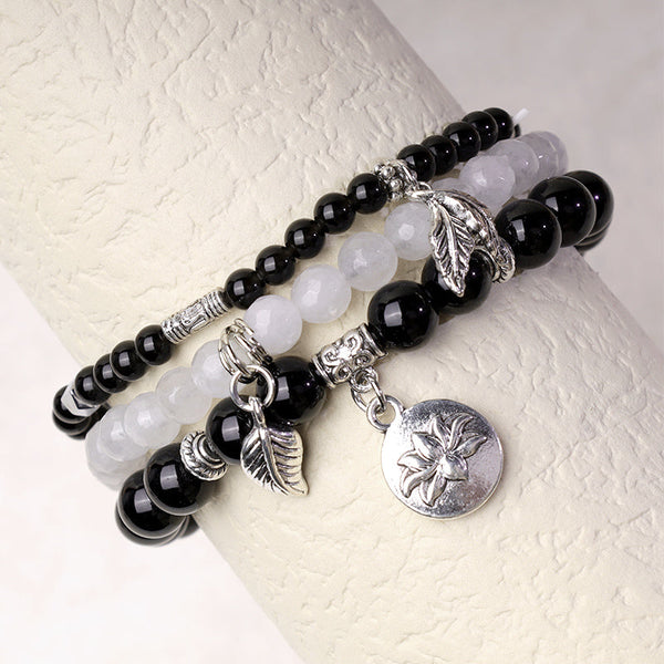 Crystal Lotus Bracelet – glossy black onyx and frosted white quartz on display stand with silver charms, stacking jewelry