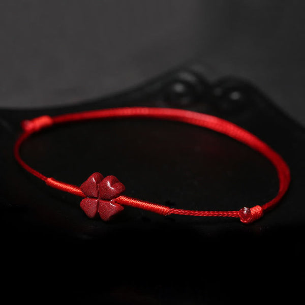 Cinnabar PiXiu Lotus Koi Fish Blessing Braid Bracelet – four-leaf clover design resting on black reflective surface, cinnabar handmade craft