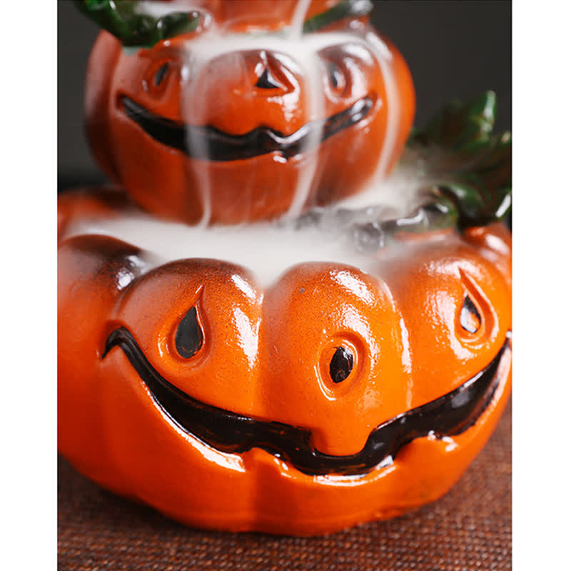 Two-tier pumpkin backflow burner close-up, white smoke pooling in carved jack-o-lantern basin, glossy orange, green stems – backflow incense holder