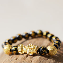 FengShui PiXiu Obsidian Bracelet – closeup on light wood surface beige background, gold PiXiu obsidian