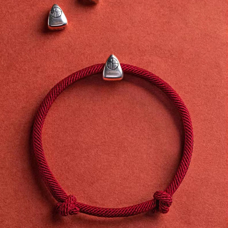 925 Silver Fu Character Braided Bracelet – Red braided cord bracelet with fortune charm and sliding knot closure on red textured surface, low side angle macro detail