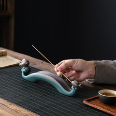 Double Koi Fish Mountain Incense Burner - hand placing incense into teal koi holder beside tea cup
