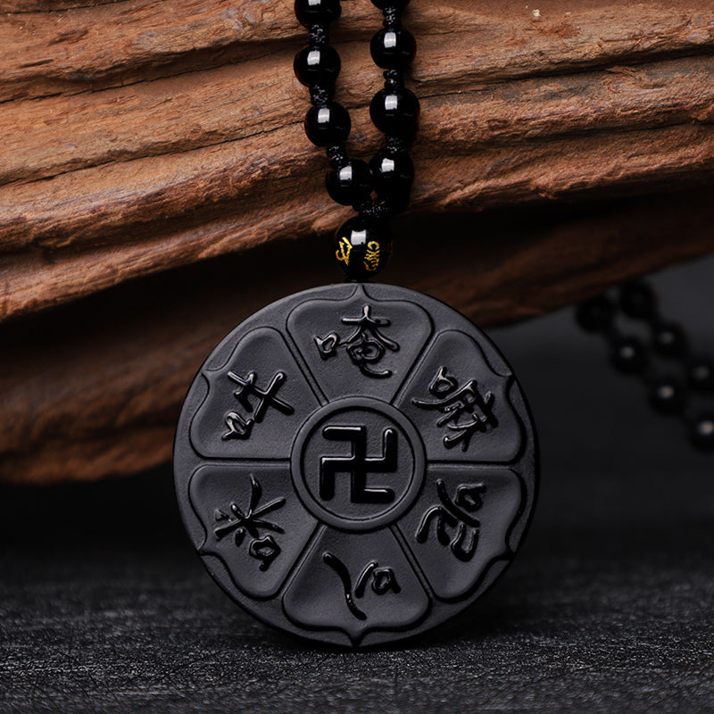 Black Obsidian Swastika Mantra Necklace - Low angle on slate, glossy obsidian pendant with wood backdrop, Buddhist jewelry