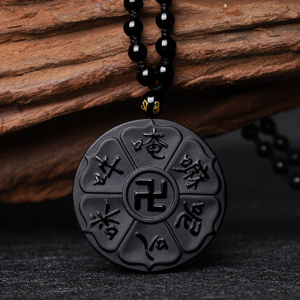 Black Obsidian Swastika Mantra Necklace - Low angle on slate, glossy obsidian pendant with wood backdrop, Buddhist jewelry