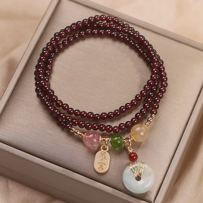 Garnet triple-strand bracelet with zhao cai wealth attraction tag and jade peace buckle pendant on champagne satin interior of premium jewelry gift box display