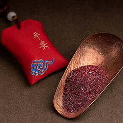 Red Sandalwood Car Hanging – Red silk amulet pouch beside copper scoop with cinnabar granules on dark textured surface