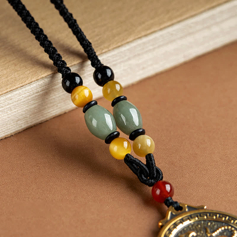 12 Chinese Zodiac Fortune Necklace Pendant – Close-up of zodiac necklace beaded section, celadon green jade oval beads, golden amber round beads, black onyx spacers, carnelian red accent, black braided cord knot work, warm brown background, artisan jewelry detail