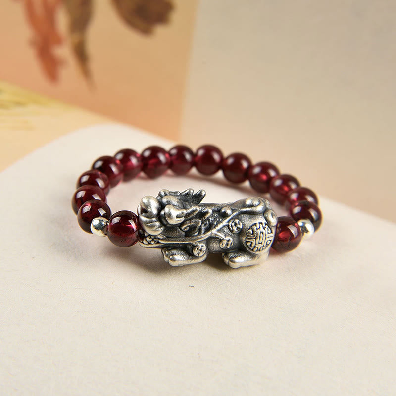 Silver Garnet PiXiu Ring – Close-up of oxidized silver PiXiu with garnet beads on cream surface