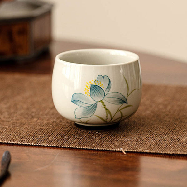 Hand Painted Lotus Tea Cup – on woven jute mat with dark wood table, blue lotus, crackle glaze, rustic zen