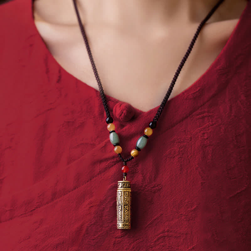 Tibetan brass cylinder pendant necklace with jade beads worn on model, ethnic prayer scroll design on black braided cord with red garment