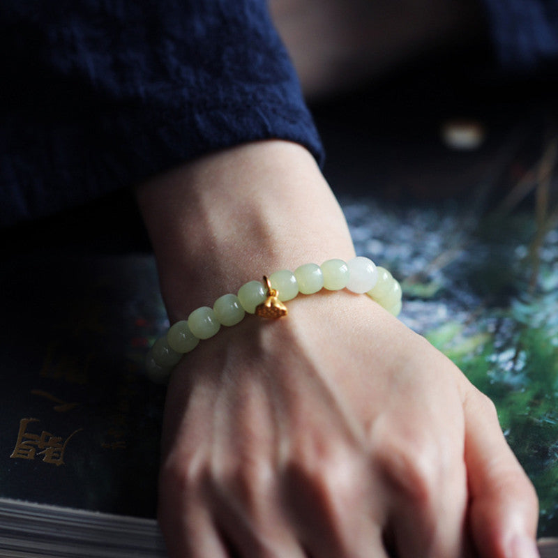 Jade Lotus Abundance Bracelet – On wrist with gold lotus bloom charm, dark reflective surface, green jade