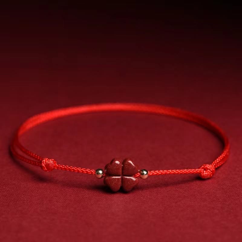 Natural cinnabar four leaf clover red string bracelet with carved vermilion charm gold spacer beads and adjustable sliding knot on red velvet fabric background