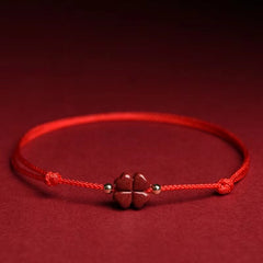 Natural cinnabar four leaf clover red string bracelet with carved vermilion charm gold spacer beads and adjustable sliding knot on red velvet fabric background