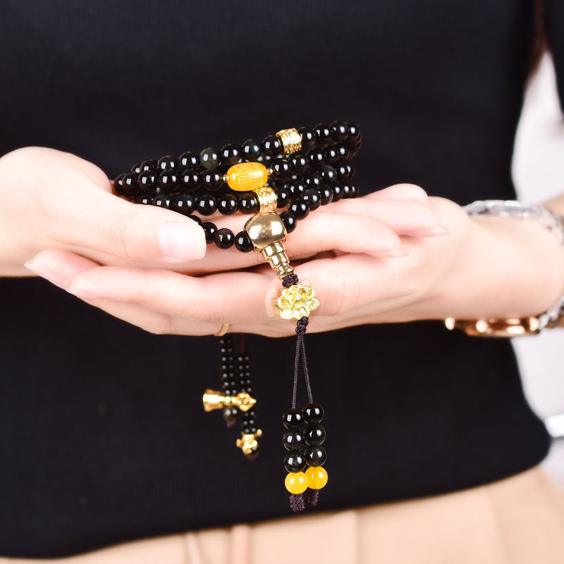 Black Obsidian Lotus Mala Bracelet - Cupped in hands showing gold hardware and amber bead, black obsidian mala