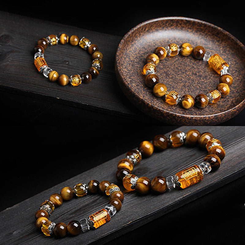 Tiger eye beaded bracelet shown in two arrangements on dark wood surface with aged ceramic dish, featuring carved amber focal bead and silver filigree spacers