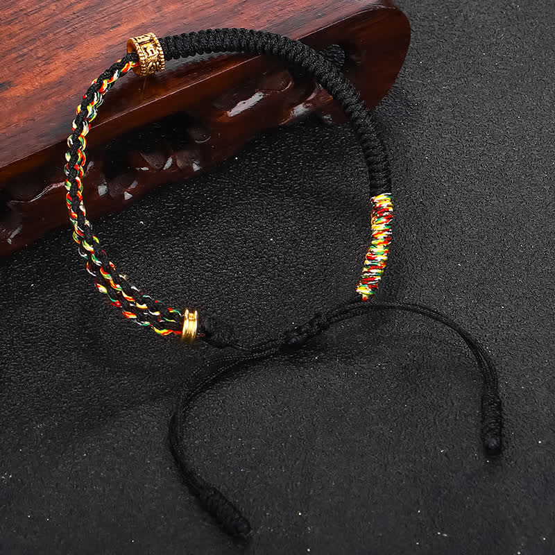 Om Mani Padme Hum Red String Bracelet – Black and multicolor woven bracelet with gold carved spacers on black matte background with carved wood prop