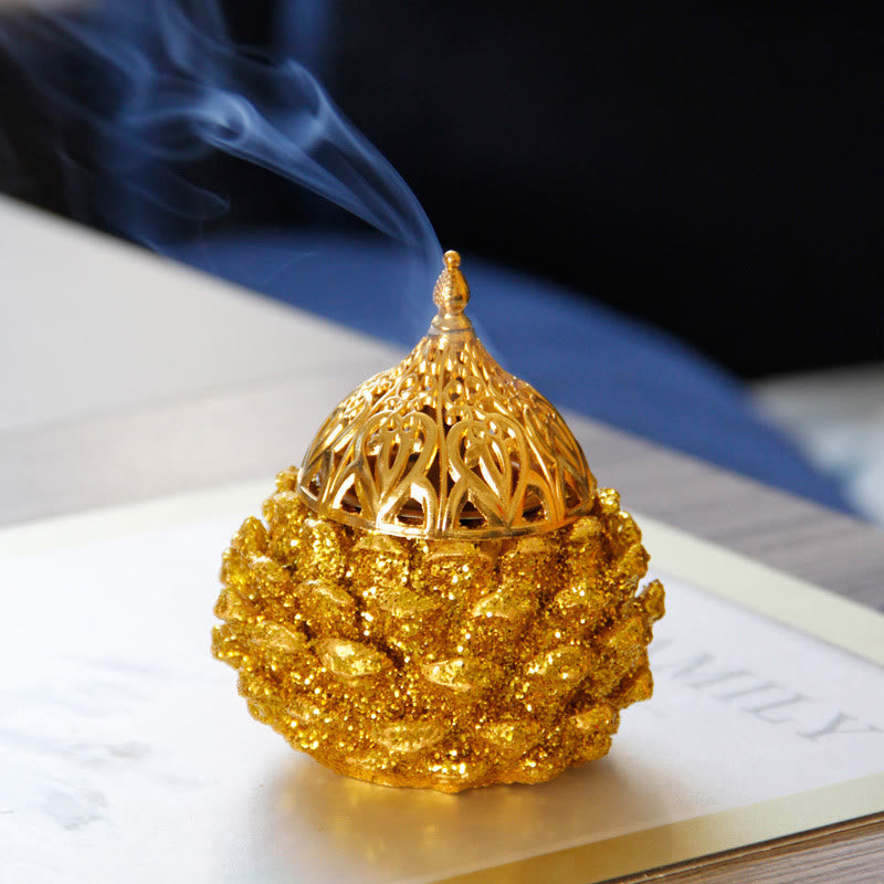 Gold Pine Cone Mini Incense Burner - Smoke rising from dome lid on glitter base, book, serene ambiance