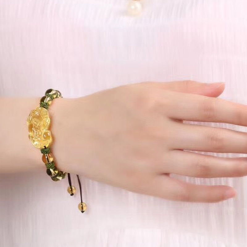 Natural Citrine PiXiu Wealth Bracelet – worn on wrist showing golden-yellow citrine beads and PiXiu centerpiece on olive green macrame cord with adjustable closure, lifestyle shot demonstrating fit and natural drape, soft pinkish background