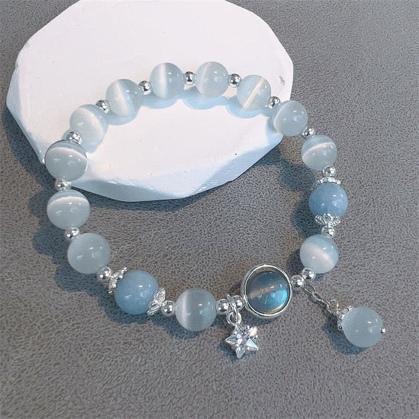 Cat's Eye Moonstone Butterfly Bracelet – Translucent white and pale blue beads with iridescent cabochon and star charm on white stone slab gray surface