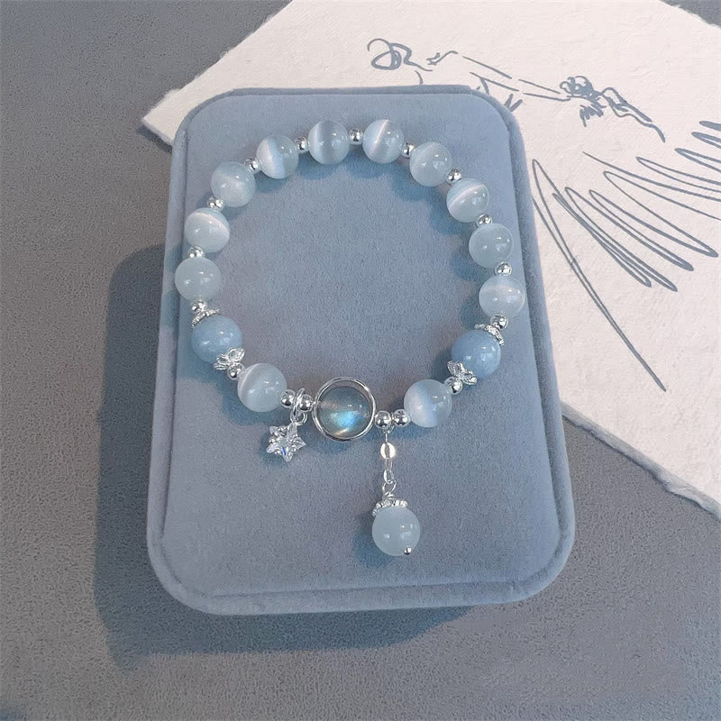 Cat's Eye Moonstone Butterfly Bracelet – Blue white cat's eye beads with moonstone center and star charm on gray-blue velvet tray with calligraphy paper, overhead