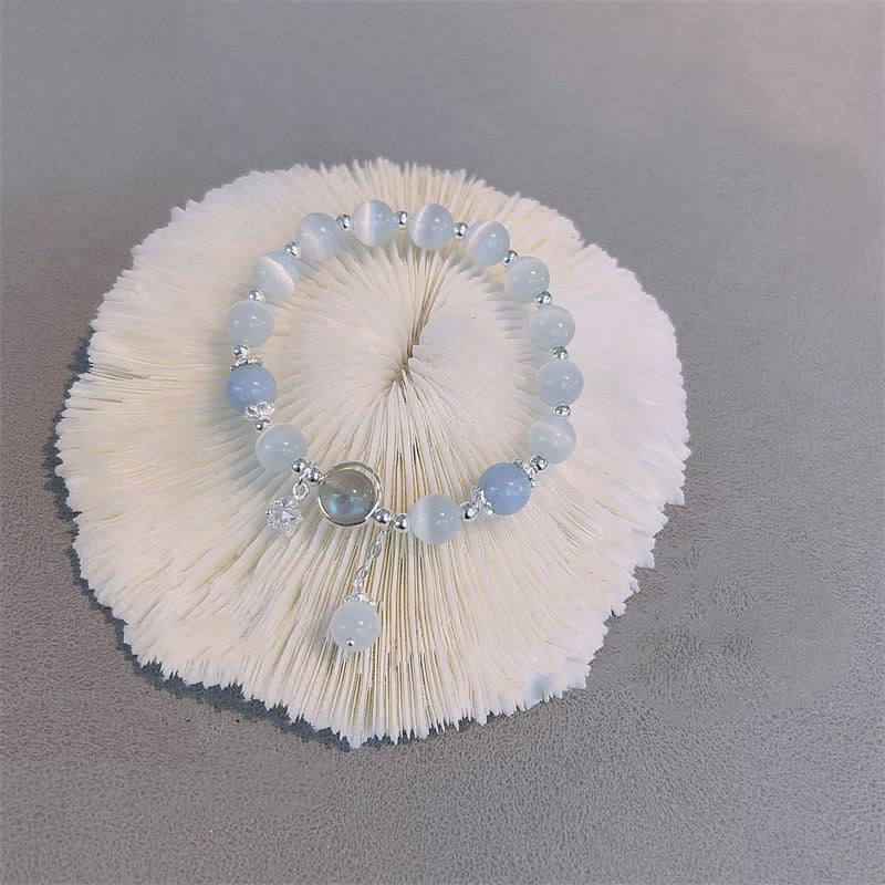 Cat's Eye Moonstone Butterfly Bracelet – Blue and white cat's eye beads with iridescent center cabochon and dangle charm on white pleated paper fan, gray surface