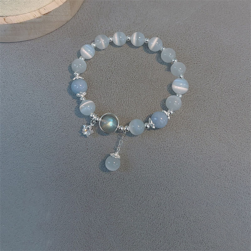 Cat's Eye Moonstone Butterfly Bracelet – Blue and white beads with dark iridescent cabochon star charm and dangle on gray mat with wood slice prop, overhead angle