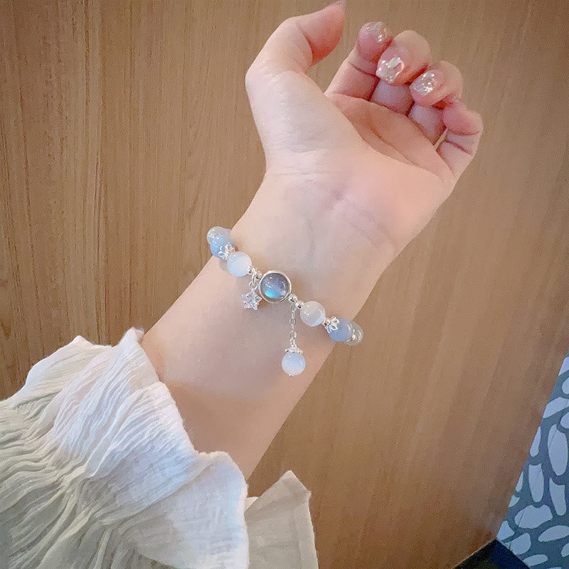 Cat's Eye Moonstone Butterfly Bracelet – Blue white opalescent beads with iridescent center and dangle charm worn on wrist with glitter nails, warm wood grain