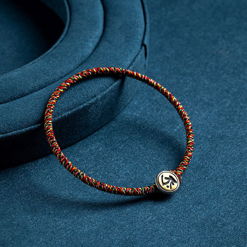 Chinese Zodiac Natal Buddha Bracelet – Multicolor cord with gold circular zodiac charm on curved velvet jewelry stand, dark blue background