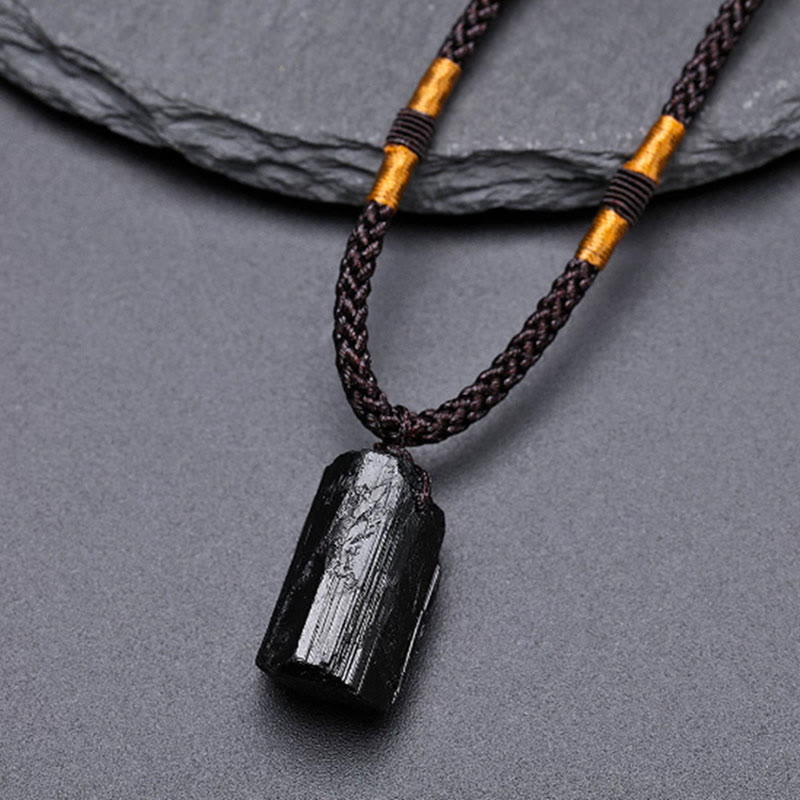 Obsidian Energy Balancing Necklace – Polished black tourmaline pendant on dark brown cord with gold tube bead and white accent bead, gray stone surface