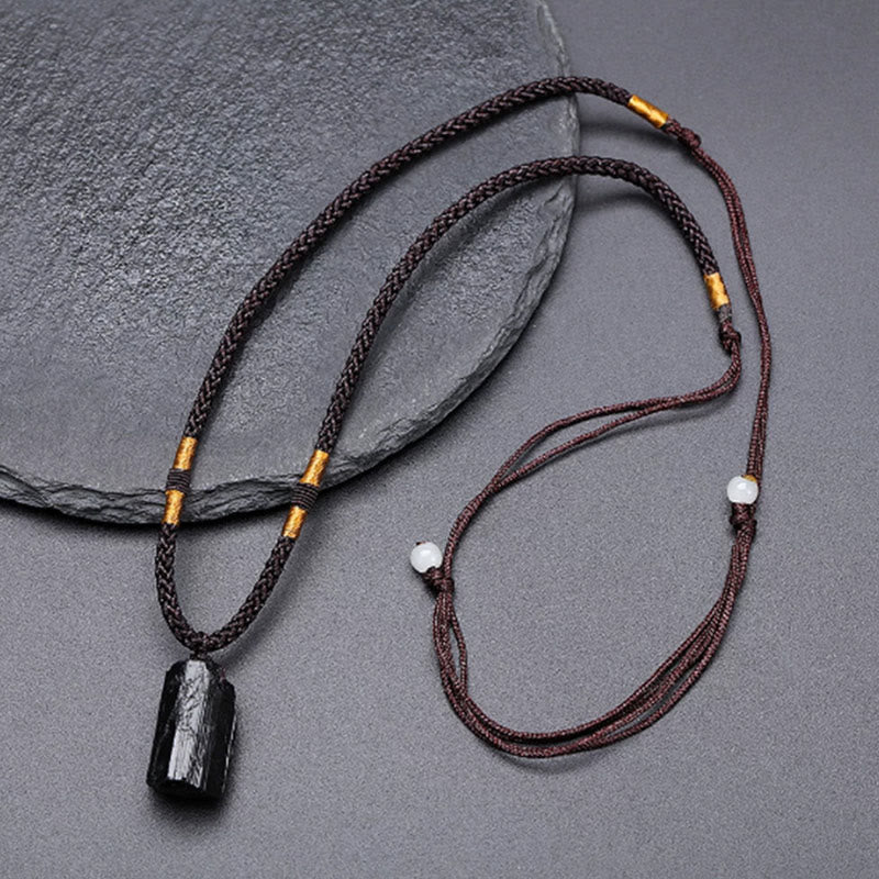 Obsidian Energy Balancing Necklace – Black tourmaline pendant on braided brown cord with gold tube and white bead, overhead flat lay on gray textured stone