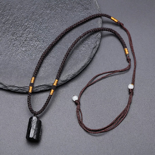 Obsidian Energy Balancing Necklace – Black tourmaline pendant on braided brown cord with gold tube and white bead, overhead flat lay on gray textured stone