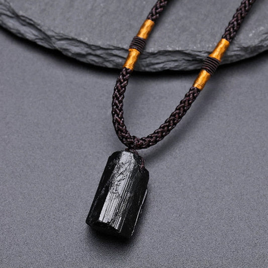 Obsidian Energy Balancing Necklace – Polished black tourmaline pendant on dark brown cord with gold tube bead and white accent bead, gray stone surface
