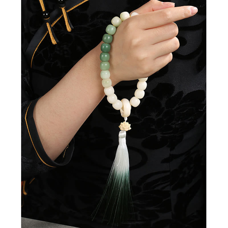 Bodhi Seed Lotus Wisdom Wrist Mala – Bracelet in prayer gesture hands, dark brocade background, lotus charm and green ombre tassel