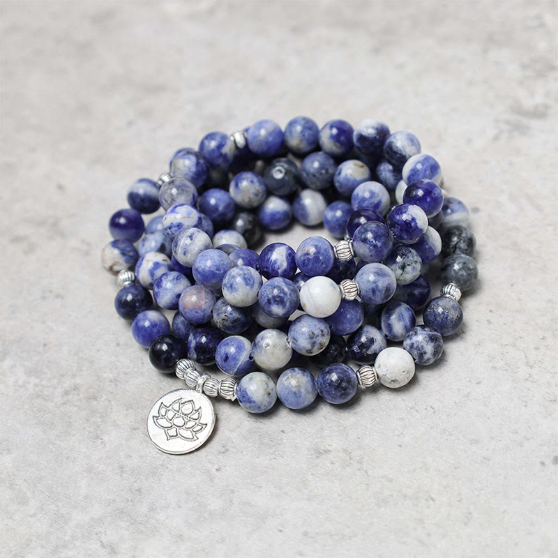 Blue Aventurine Lotus Peace Bracelet – layered wrap bracelet spiral with lotus pendant, blue and white stone mala on textured gray surface