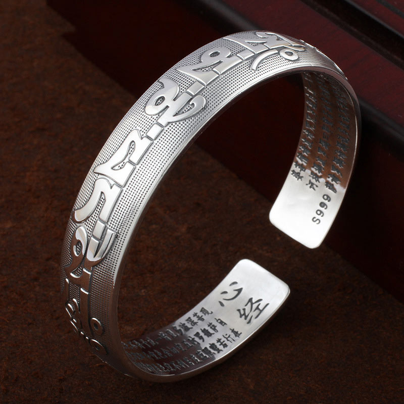 Tibetan Om Mani Padme Hum silver prayer bangle with raised Tibetan script exterior, Heart Sutra Chinese engraving inside, S999 fine silver on dark wood.