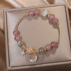 Strawberry Quartz love bracelet with pink and gray gemstone beads, gold pavé crystal crescent moon and star charms, displayed in elegant beige jewelry box.