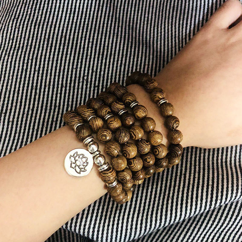 Tibetan Lightning Strike Wood Mala – worn on wrist with lotus charm over striped fabric