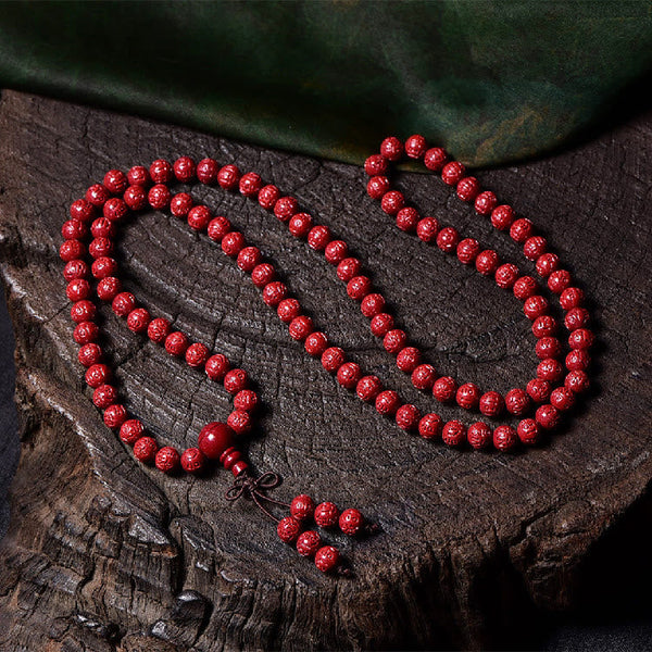 108 Mala Beads Cinnabar Bracelet – Full length flat lay on wood, red carved beads