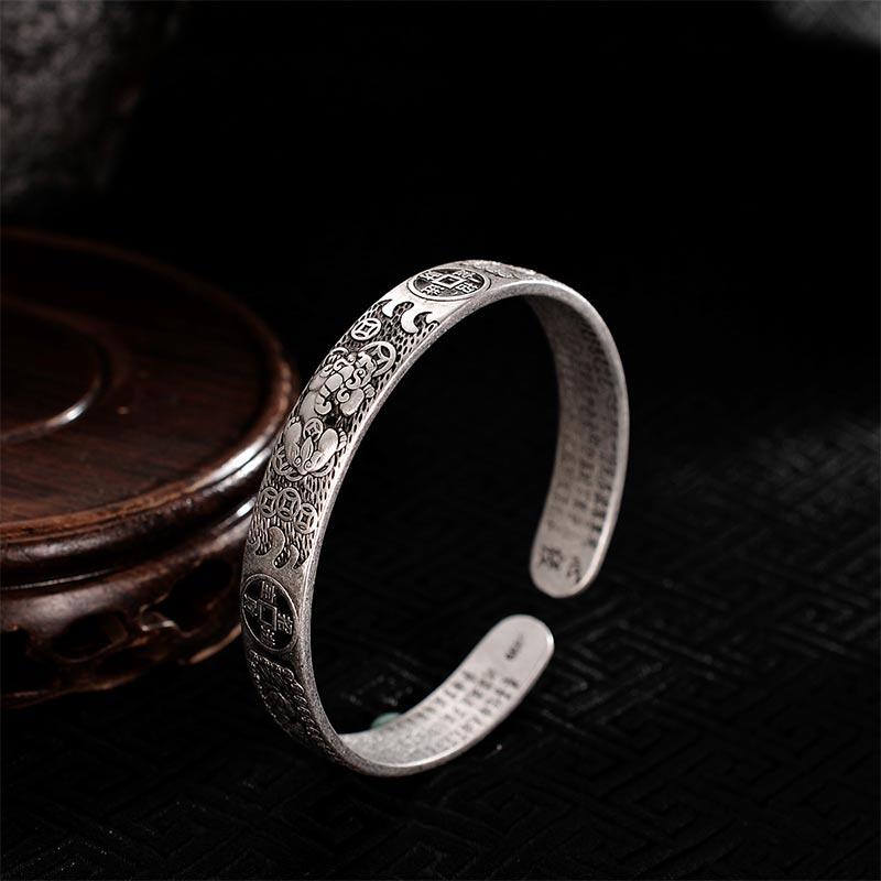 Oxidized silver feng shui bracelet with Chinese lucky coin designs, Pixiu wealth creature relief and interior sutra text on black background