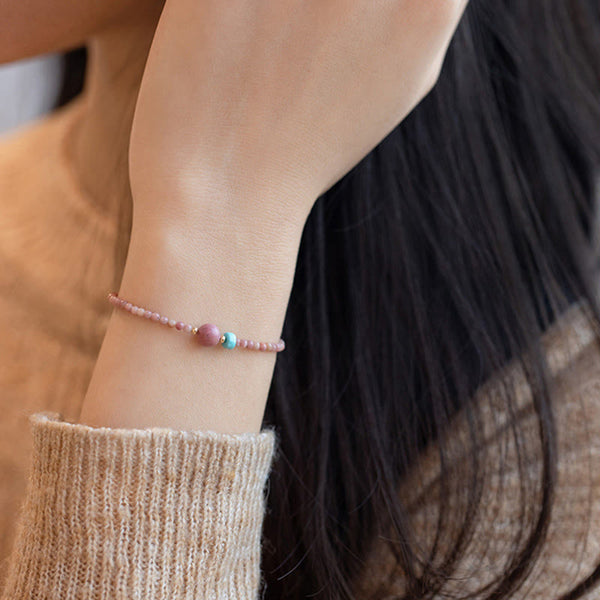 Rhodonite Loving Energy Bracelet – Pink bead bracelet with rose focal and turquoise accent worn on wrist, dark hair lifestyle close-up