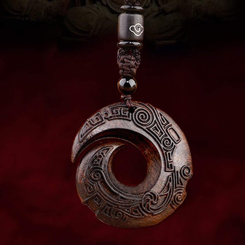 Ebony wood peace buckle pendant necklace featuring interlocking spiral eternity design with carved geometric meander patterns on dark brown hardwood with silver-inlaid cloud bead on dark cord
