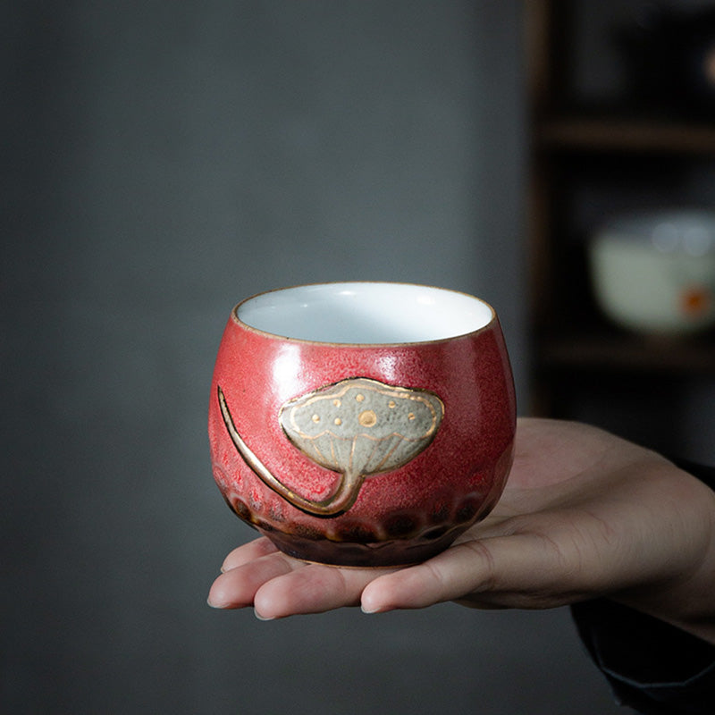 Lotus Pod Ceramic Kung Fu Tea Cup - Crimson cup with gold-seeded lotus held in palm, tea ceremony